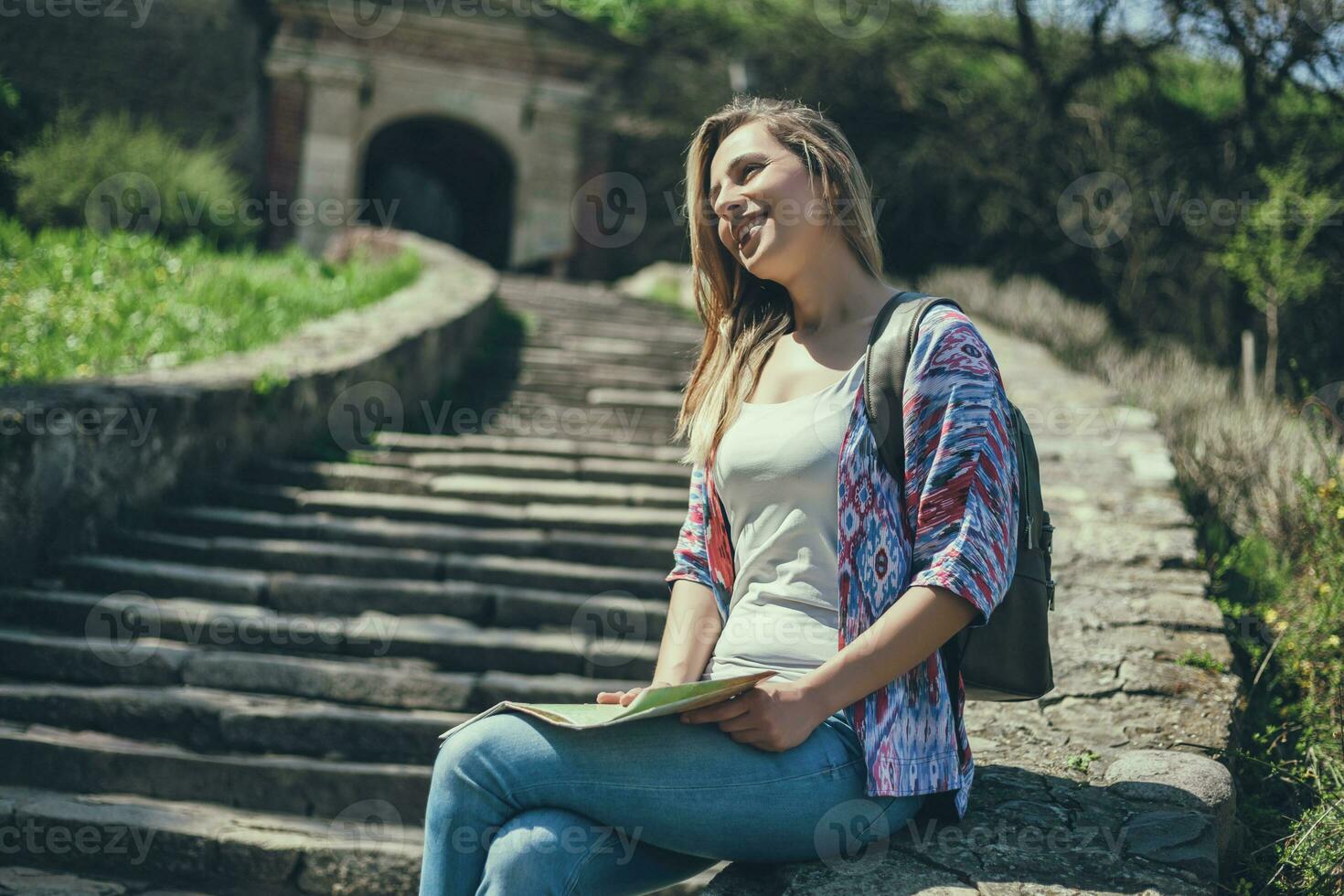 Young tourist woman sitting by the stairs with a map photo