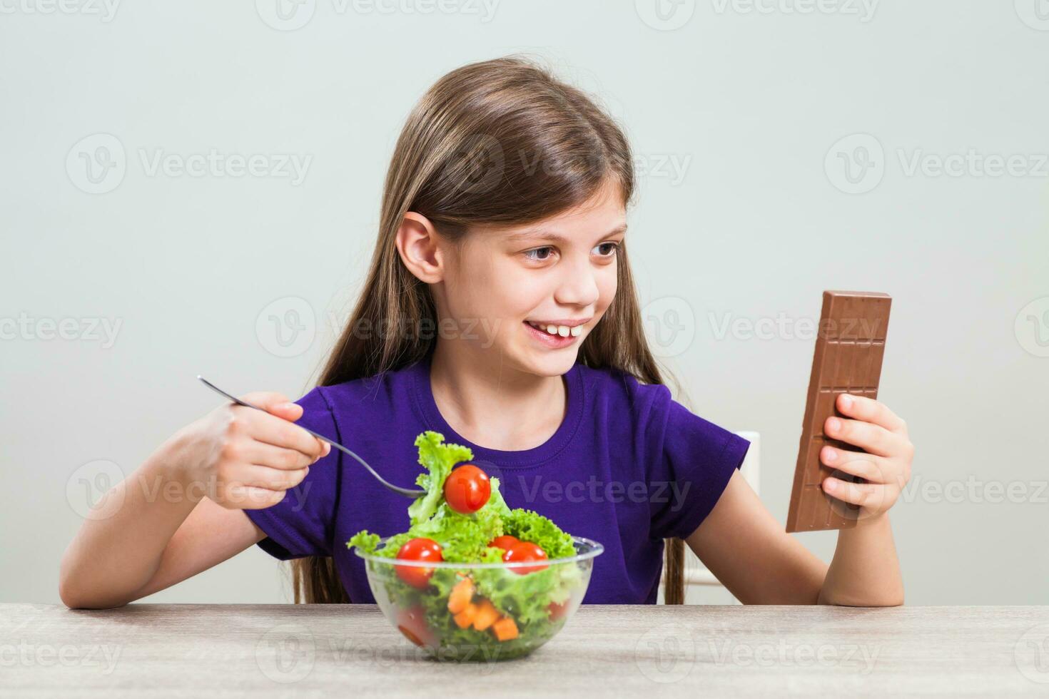 A girl choosing between salad and a chocolate bar photo