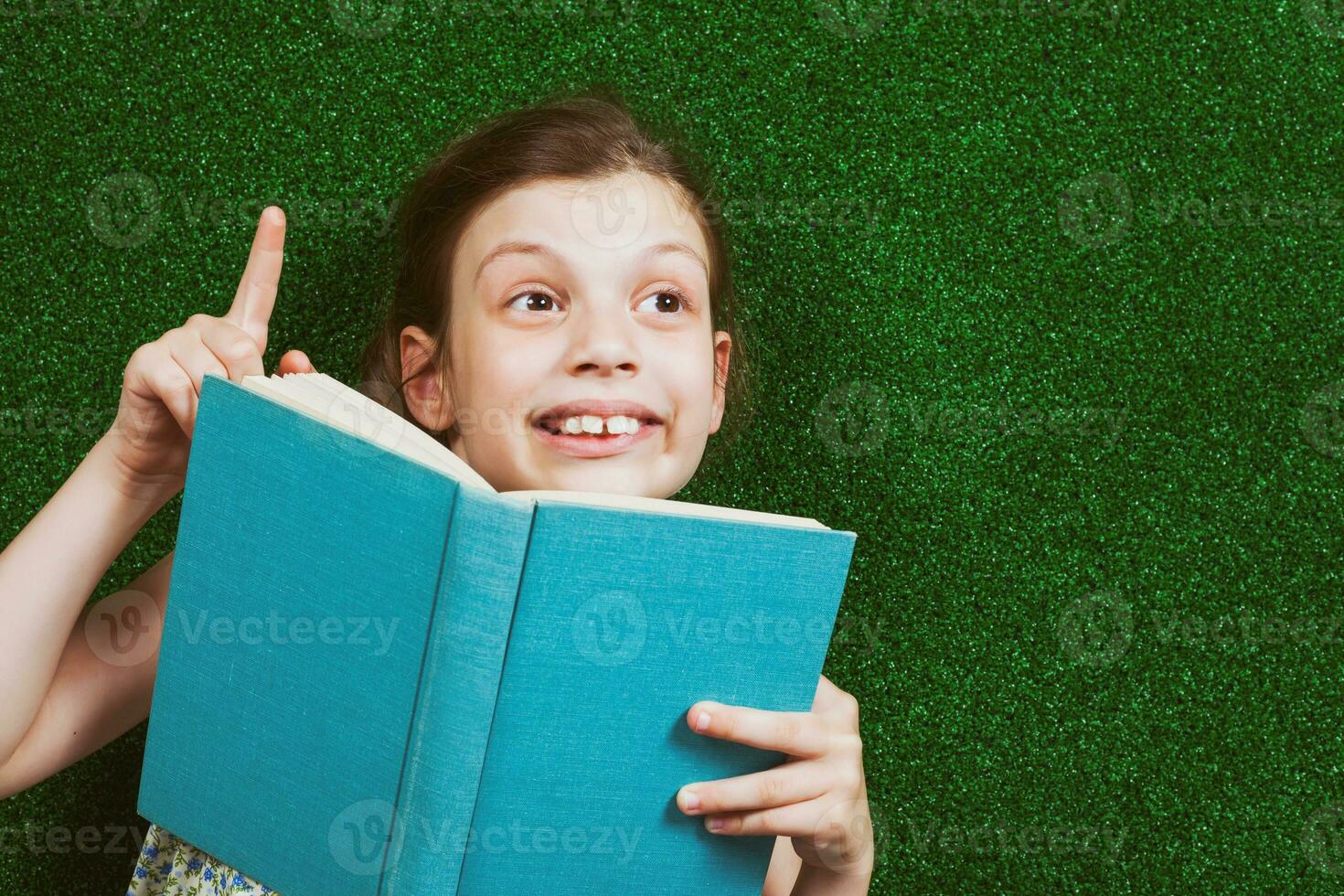 Little girl is lying on artificial grass with a book photo