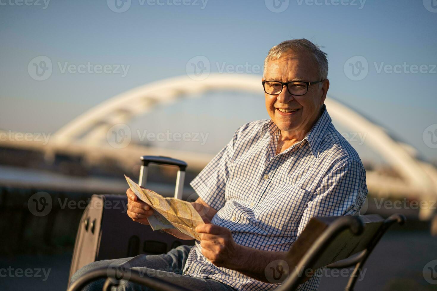 Senior man reading a map outside with a suitcase. Tourist concept photo
