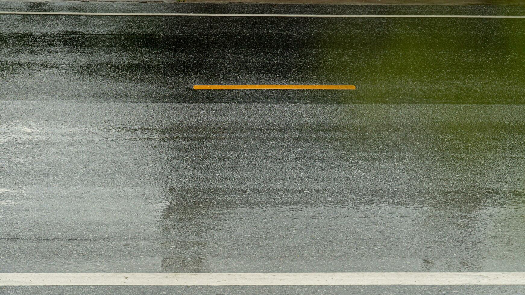 mojado de pesado lluvia en asfalto la carretera. para transporte antecedentes. cerca arriba en amarillo línea en el centrar de la carretera. foto