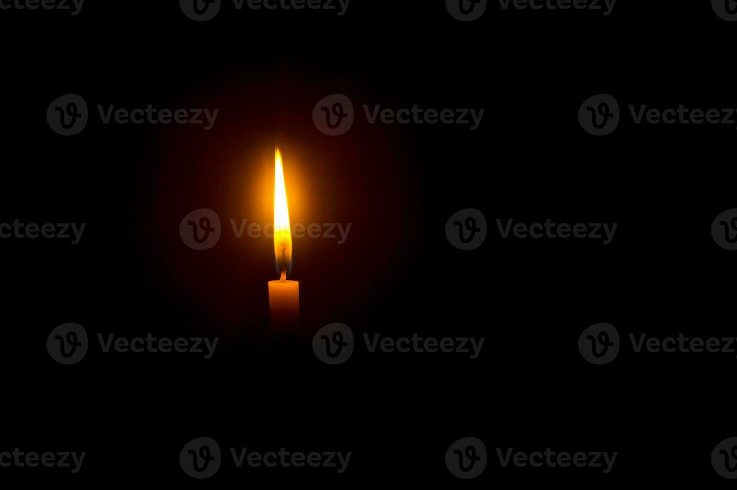 A single burning candle flame or light glowing on an orange candle on black or dark background on table in church for Christmas, funeral or memorial service with copy space photo