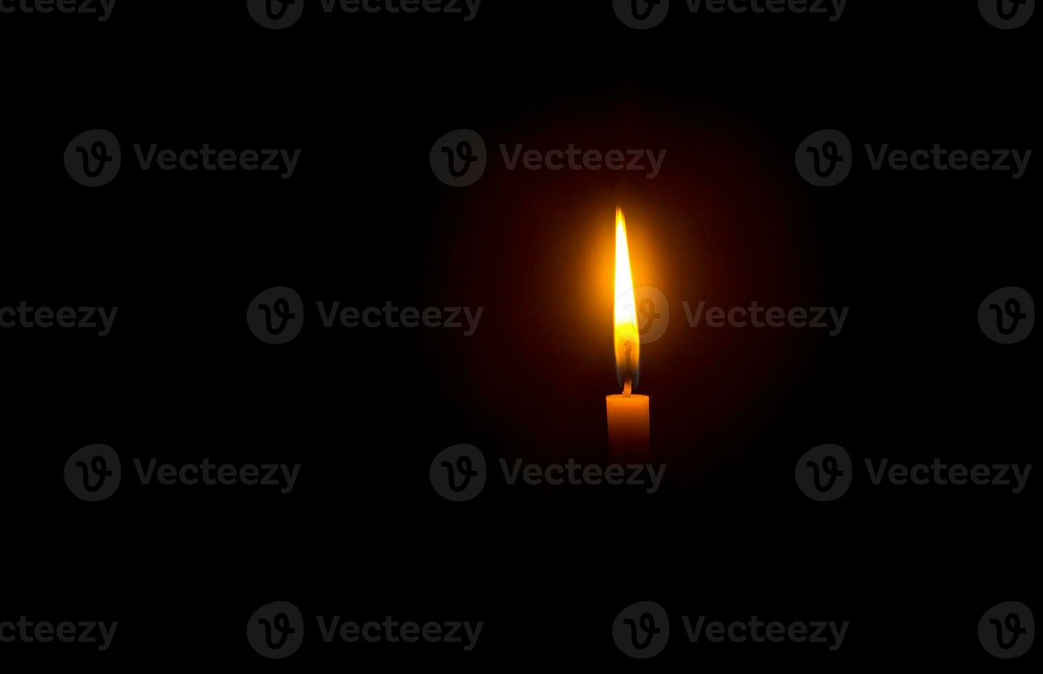 A single burning candle flame or light glowing on an orange candle on black or dark background on table in church for Christmas, funeral or memorial service with copy space photo