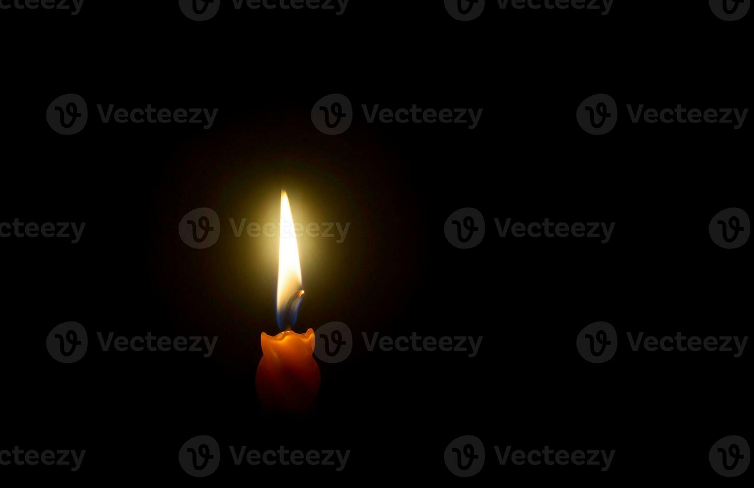 A single burning candle flame or light glowing on spiral orange candle on black or dark background on table in church for Christmas, funeral or memorial service with copy space photo