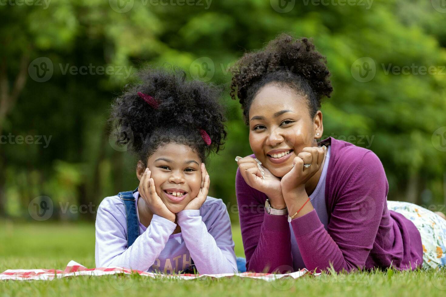 African American mother and young daughter are lying down after having a summer picnic in the public park for weekend leisure and happiness concept photo