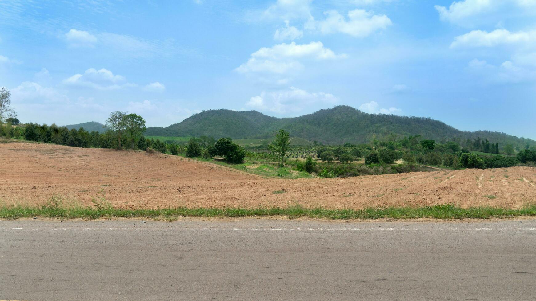 Horizontal view of asphalt road in Thailand. Background of land area prepared for agricultural cultivation. Background of garden and forest ground with mountains. Under the blue sky. photo