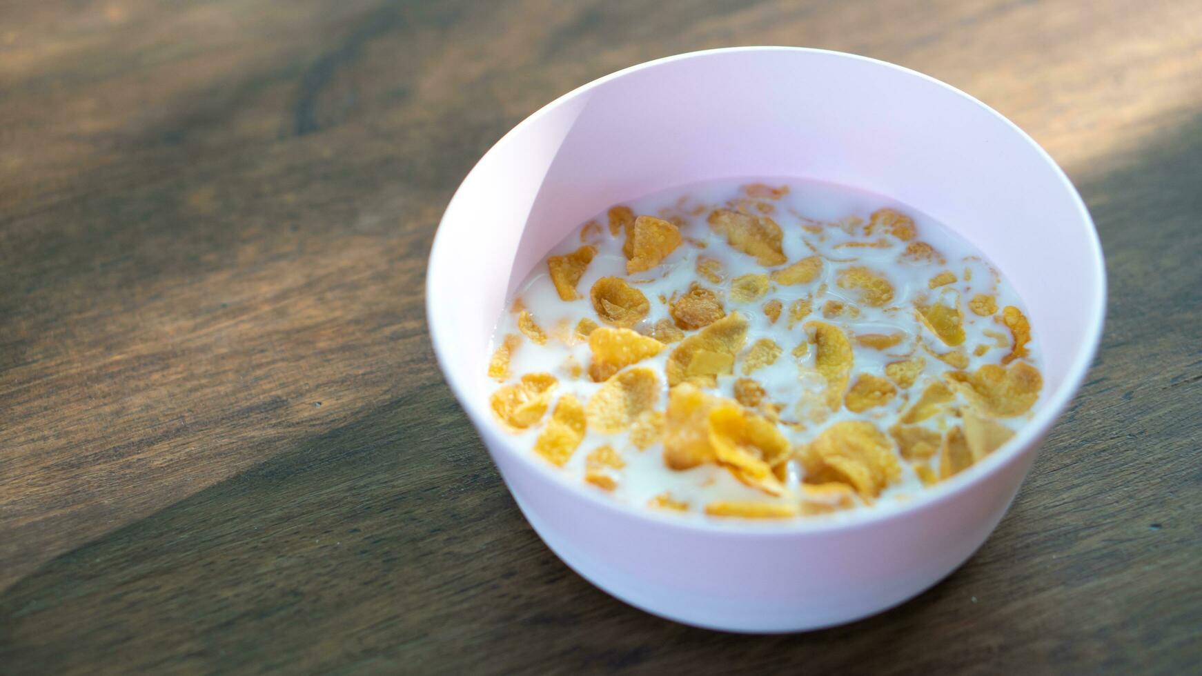 Cereal yellow pastry served with clean white cow's milk. In a pink plastic container. Laying on the morning brown wooden floor photo