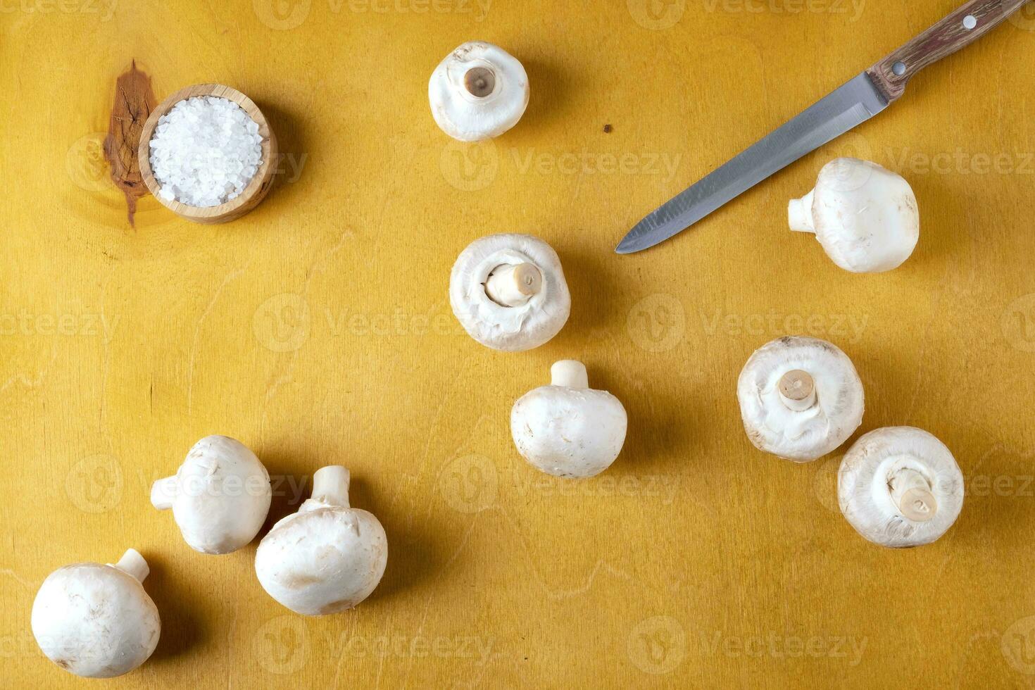 Champignon mushrooms and a kitchen knife on a yellow background photo