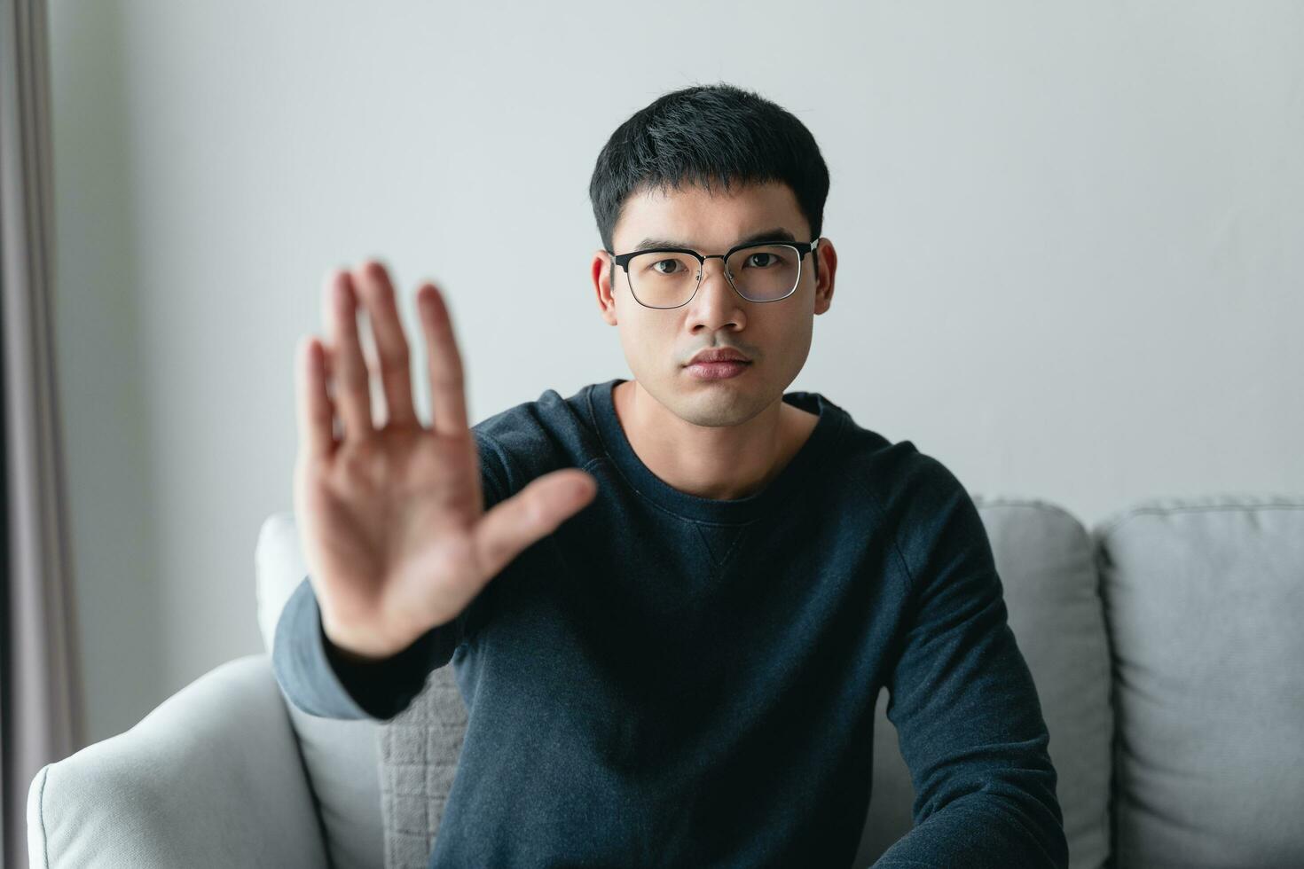 The man showing hand gesture stop sign sitting on the sofa at home. photo