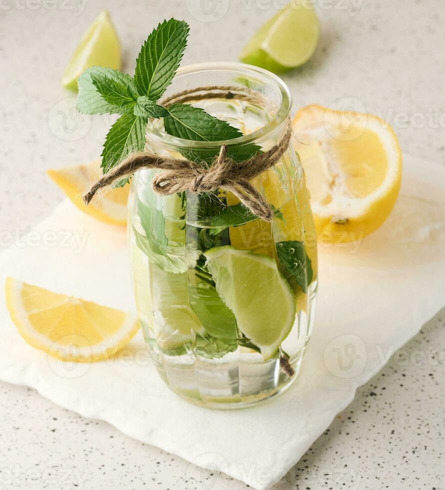 Lemonade in a transparent glass with lemon, lime, rosemary sprigs and mint leaves on a white background photo