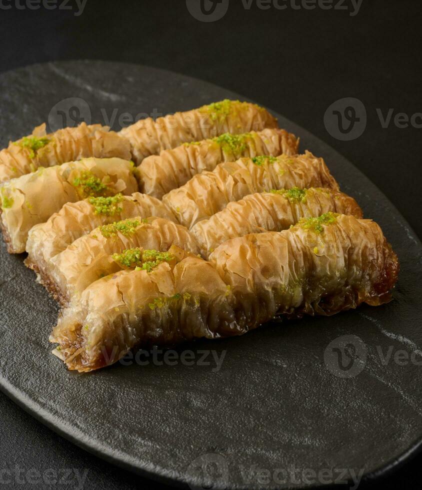 Pieces of baked baklava in honey and sprinkled with pistachios on a black board photo