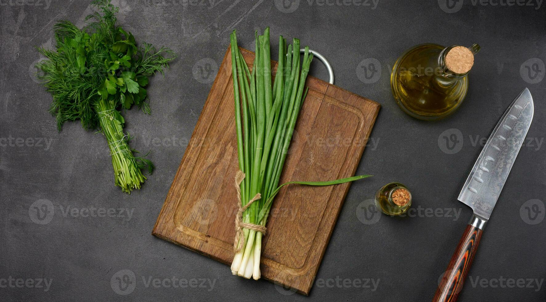 Empty wooden board, green onions, bunch of dill and parsley on a black table, top view photo