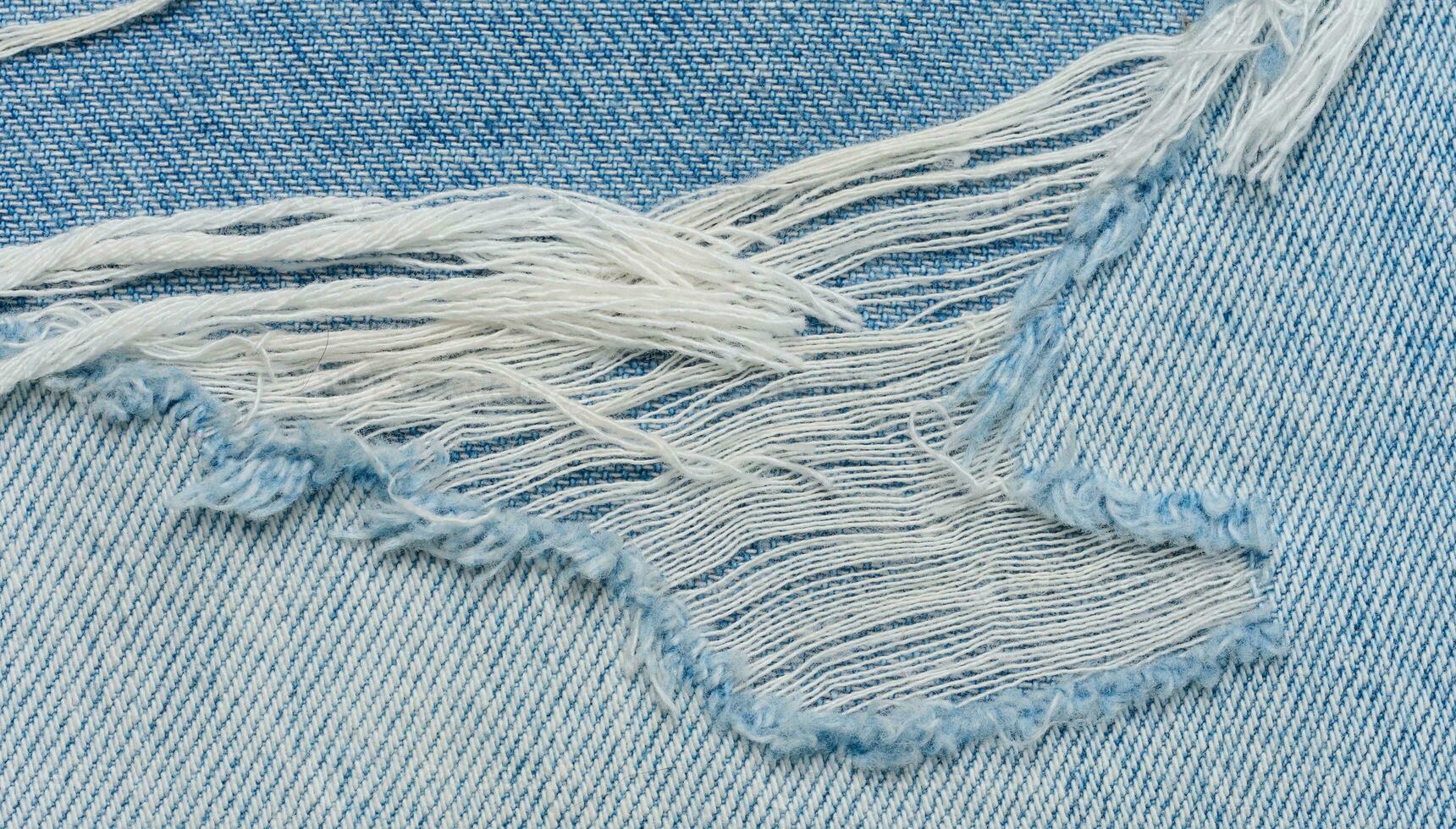 Fragment of blue jeans fabric with a hole, full frame, close up photo