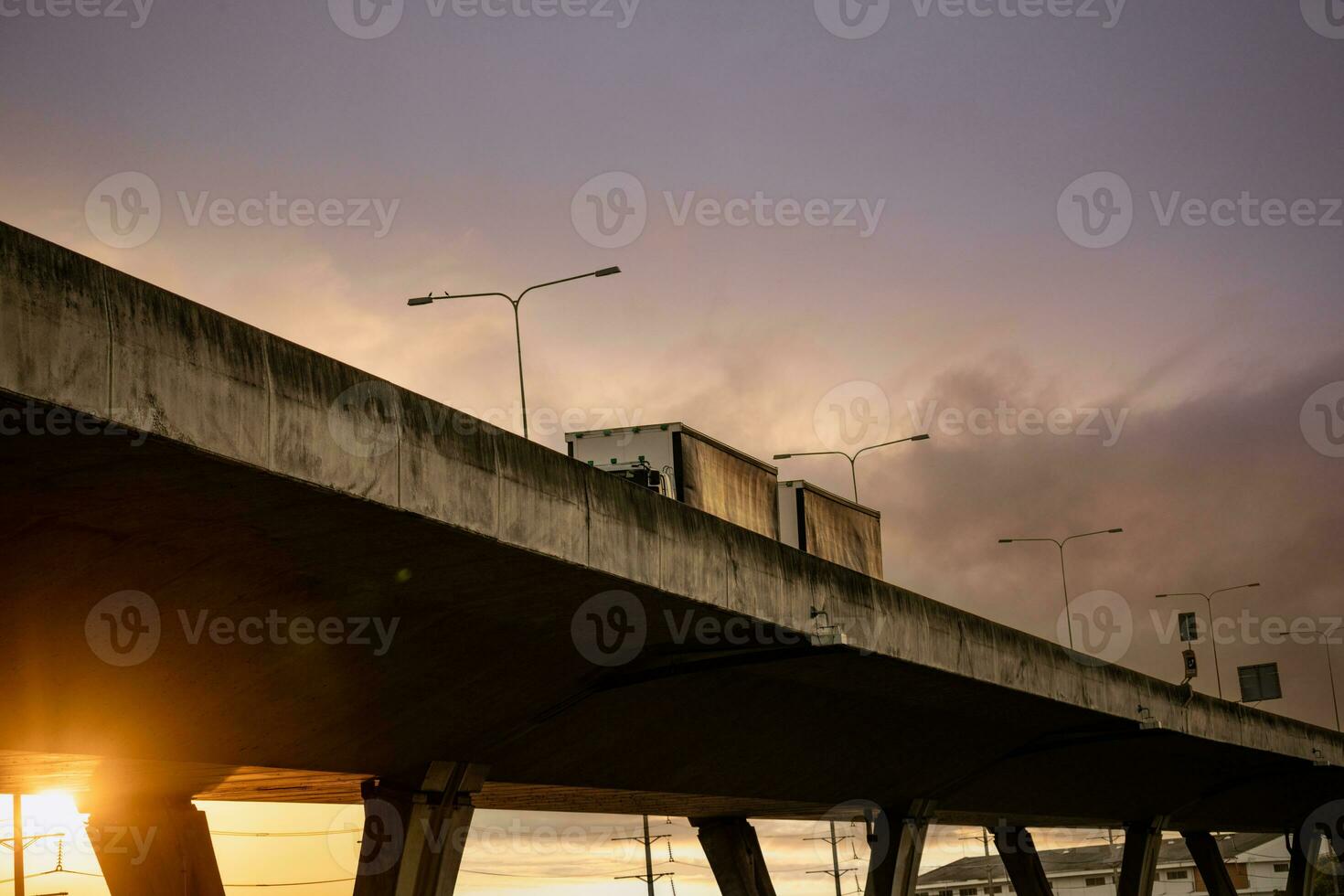 Bottom view of elevated concrete highway with truck driving. Overpass concrete road. Road flyover structure. Motorway with sunset sky. Concrete bridge engineering construction. Bridge architecture. photo