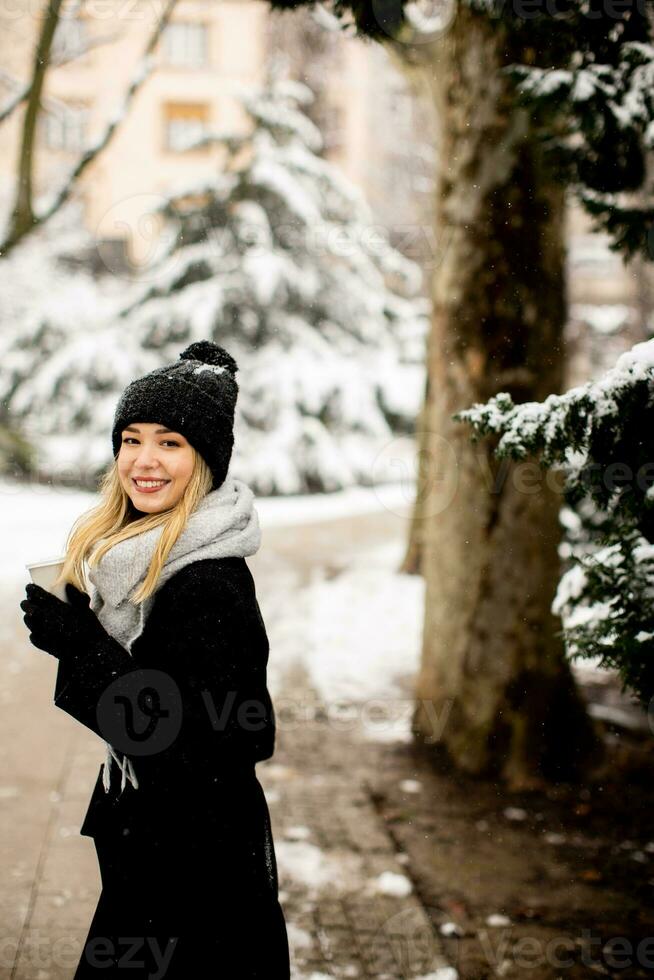 Young woman in warm clothes enjoying in snow with takeaway coffee cup photo