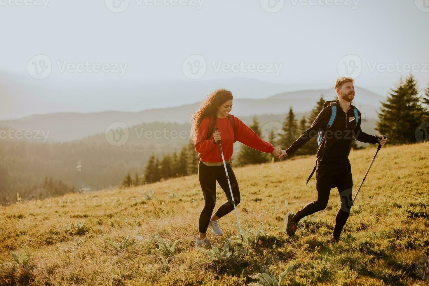 Young couple walking with backpack over green hills photo