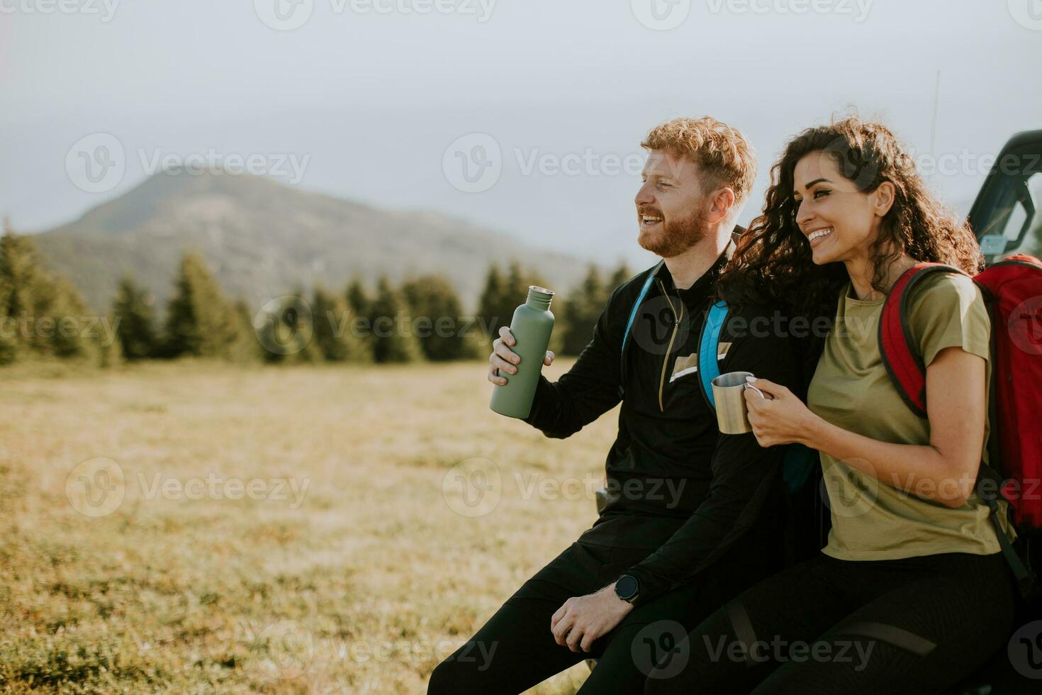 Smiling couple preparing hiking adventure with backpacks by terrain vehicle photo