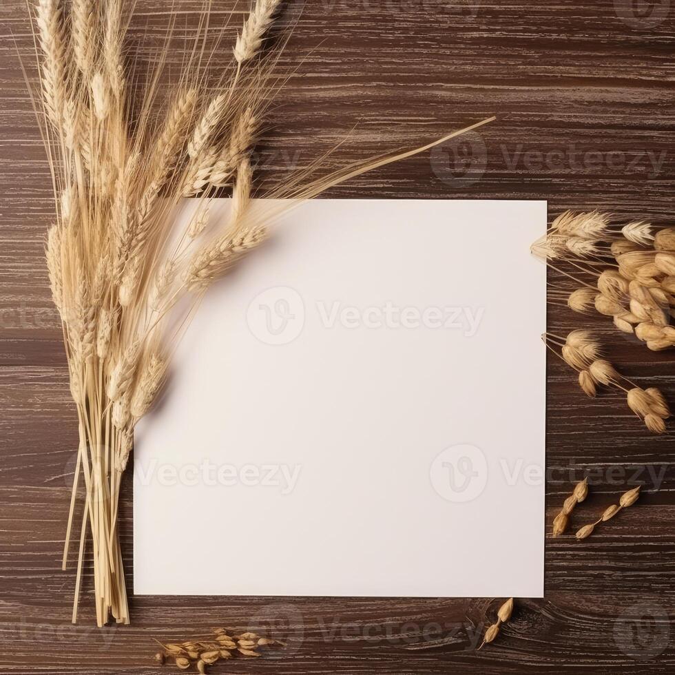 Top View of Blank White Paper with Dried Wheats on Brown Wooden Texture Background, Vintage Delicate Business or Wedding Card. . photo