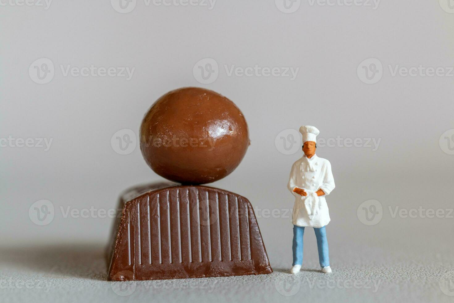 Miniature people chef with chocolate standing while standing against a gray background photo