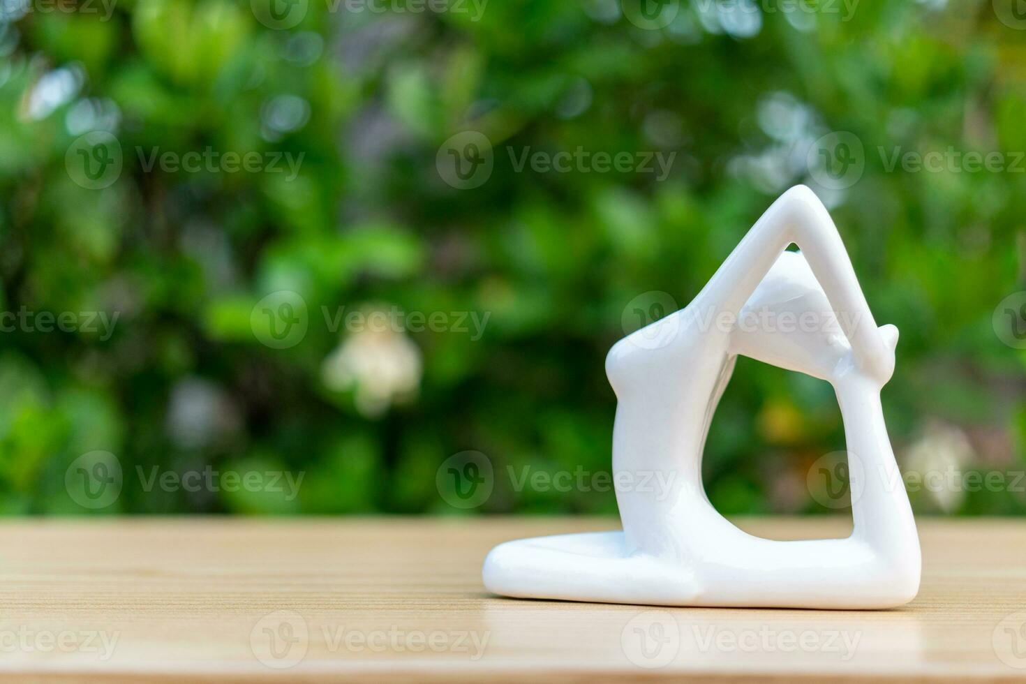 Ceramic Yoga Figurine of Woman doing yoga pose on wooden floor and green leaf  background photo