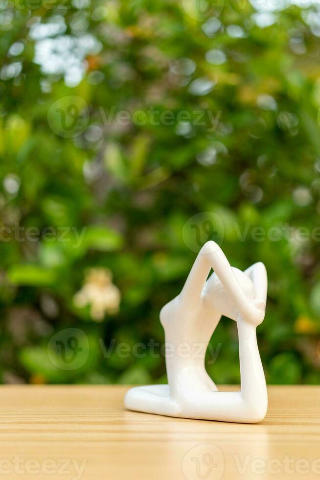 Ceramic Yoga Figurine of Woman doing yoga pose on wooden floor and green leaf  background photo