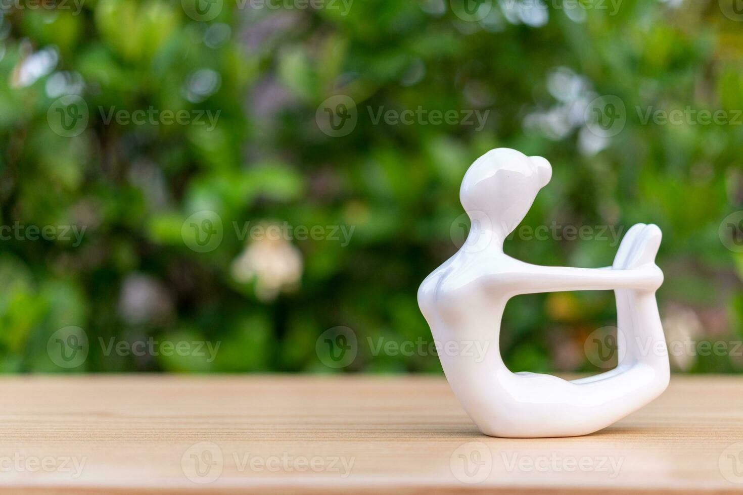 Ceramic Yoga Figurine of Woman doing yoga pose on wooden floor and green leaf  background photo