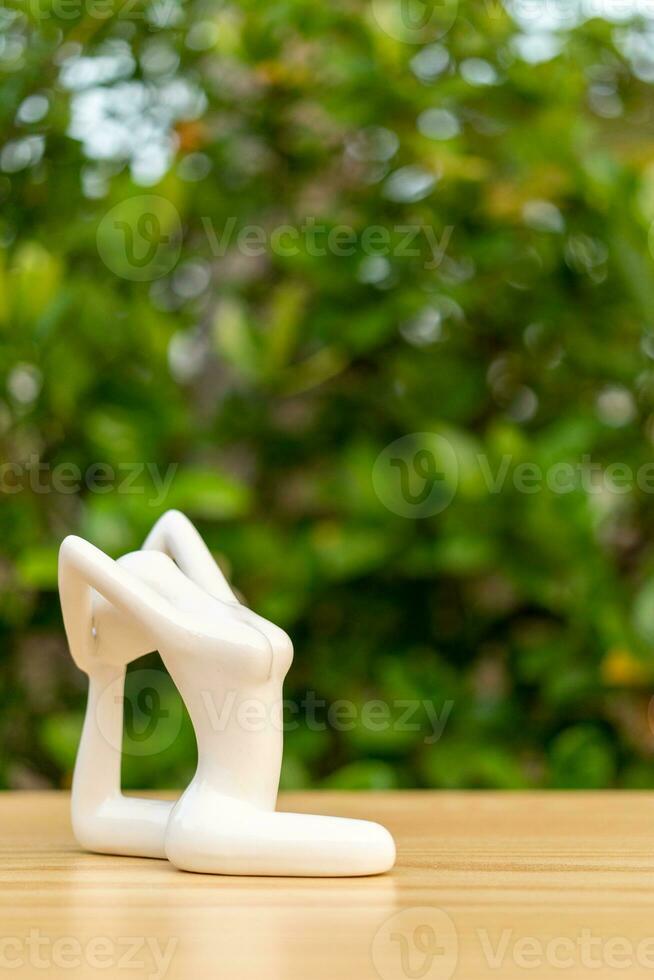 Ceramic Yoga Figurine of Woman doing yoga pose on wooden floor and green leaf  background photo