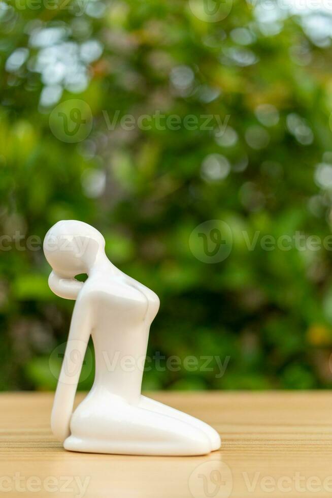 Ceramic Yoga Figurine of Woman doing yoga pose on wooden floor and green leaf  background photo