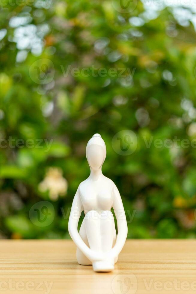 Ceramic Yoga Figurine of Woman doing yoga pose on wooden floor and green leaf  background photo