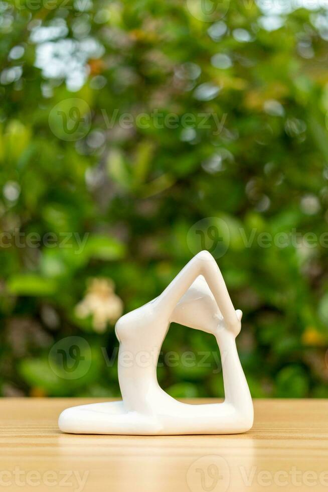 cerámico yoga figurilla de mujer haciendo yoga actitud en de madera piso y verde hoja antecedentes foto