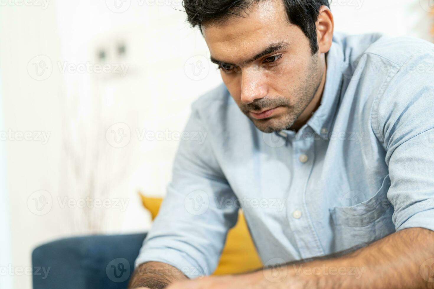 Unhappy man thinking about health or something bad on his sofa at home in the living room. upset man having problems, side view, copy space. Loneliness, depression, financial hangover concept. photo
