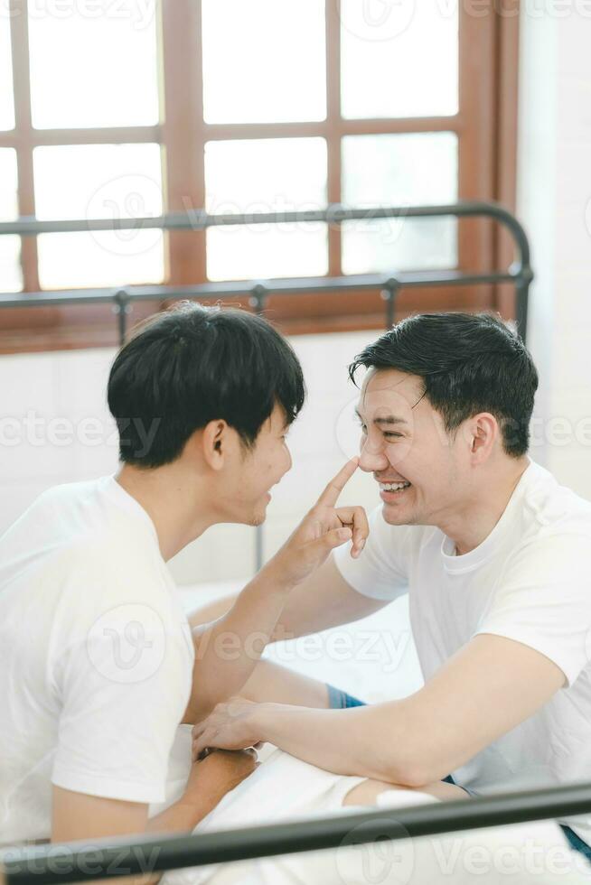 Asian gay couple touching boyfriend nose and smiling while resting at home. Cute gay couple playing in bed. LGBT lovers expressions of love concept photo