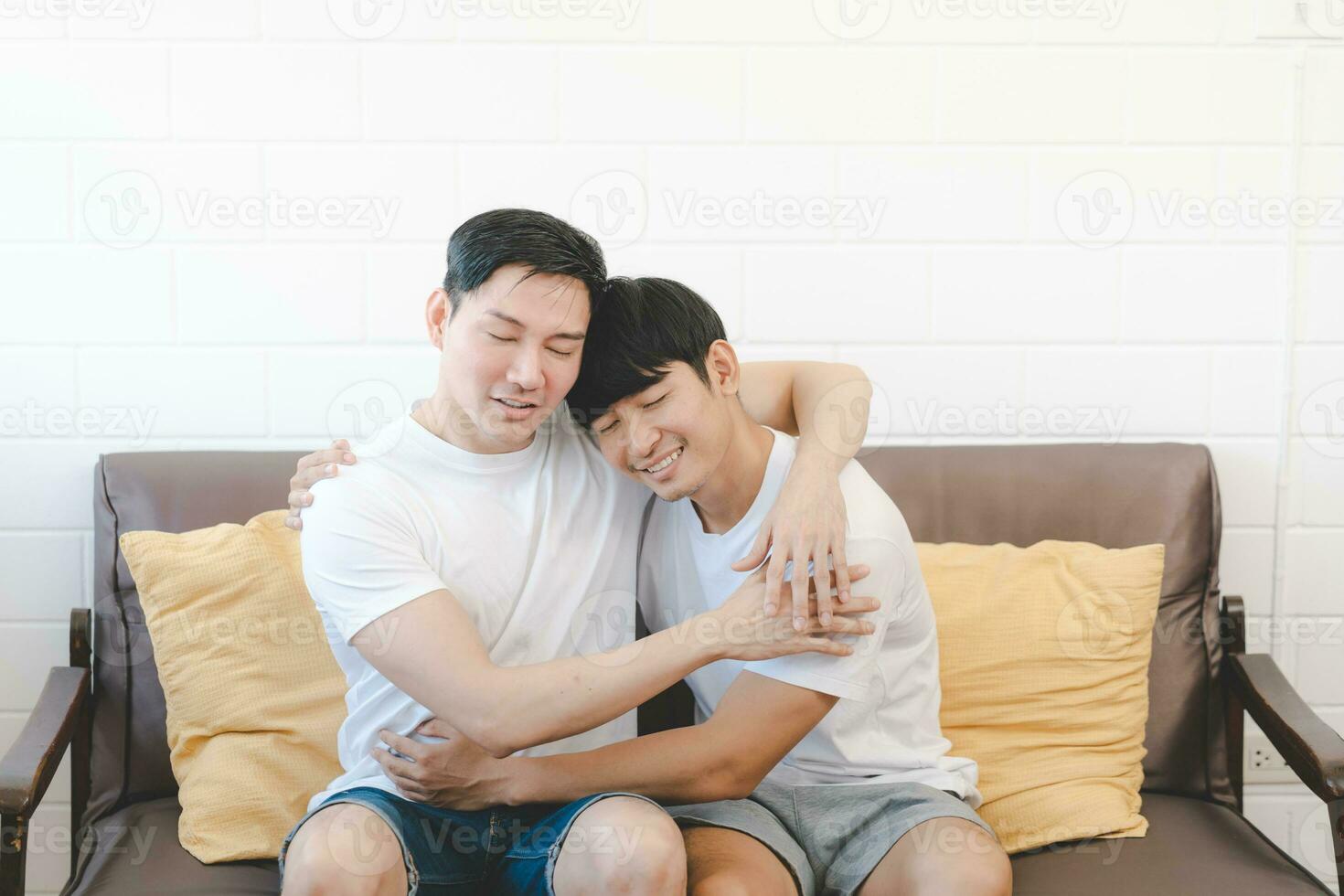 Happy Asian gay couple hug together on sofa. Asian LGBT couple embracing together at home. Diversity of LGBT relationships. A gay couple concept. LGBT multi relationship. photo