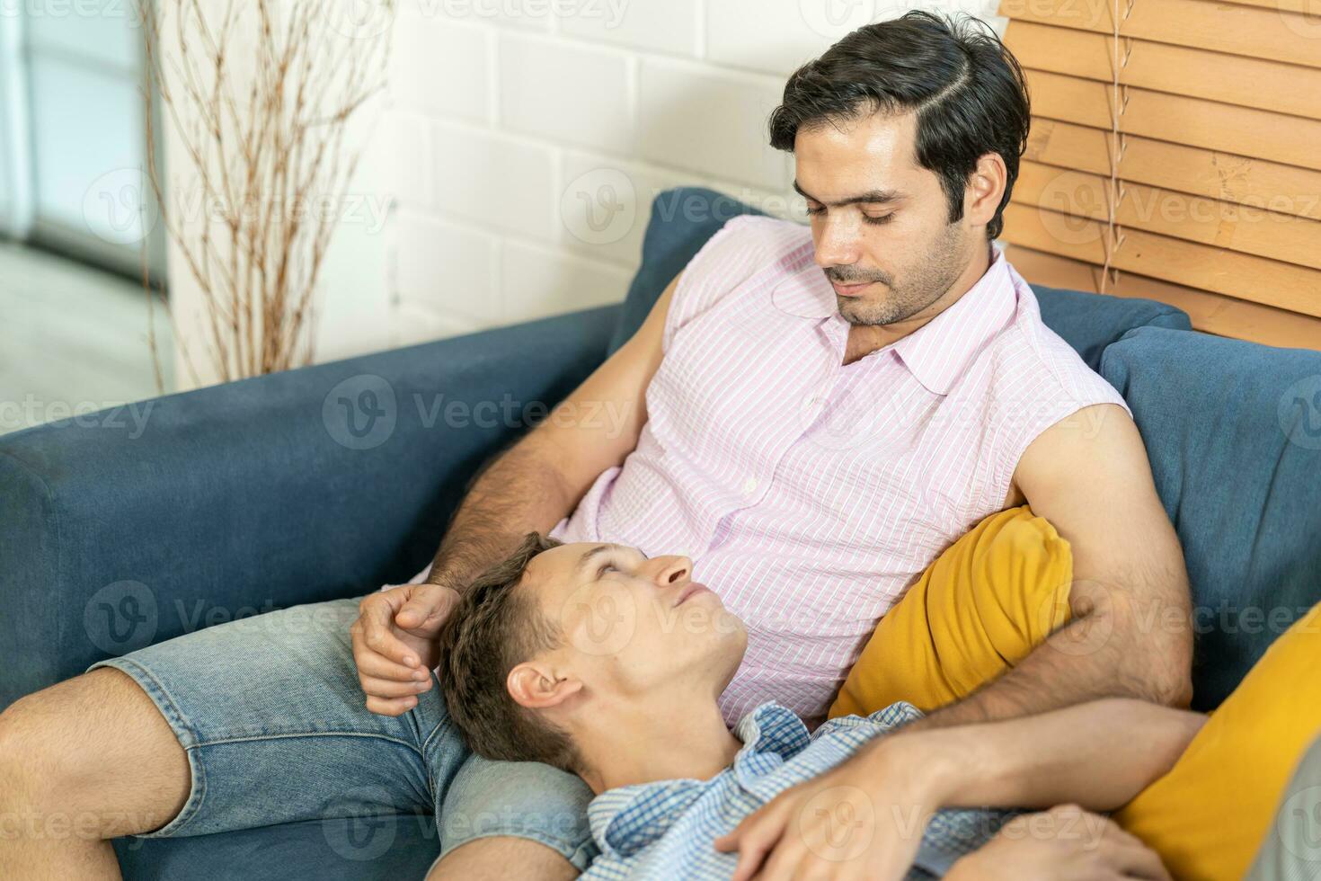 amoroso mismo sexo masculino Pareja acostado en sofá a hogar acecho televisión y relajante juntos. homosexual relación concepto. foto