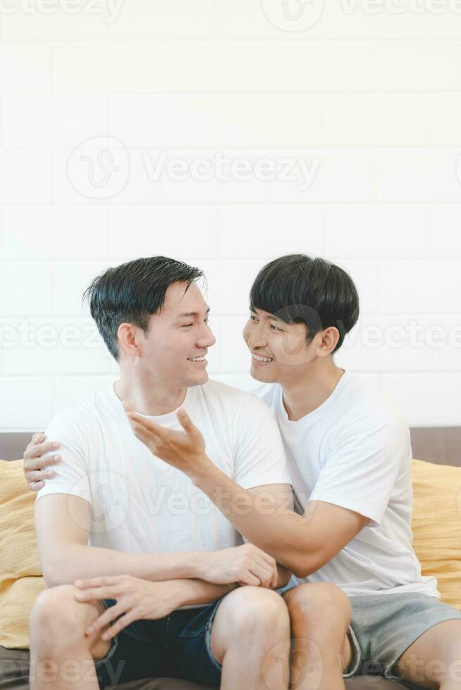 Happy Asian gay couple hug together on sofa. Asian LGBT couple embracing together at home. Diversity of LGBT relationships. A gay couple concept. LGBT multi relationship. photo