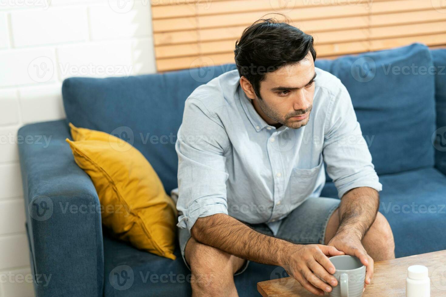 Unhappy man thinking about health or something bad on his sofa at home in the living room. upset man having problems, side view, copy space. Loneliness, depression, financial hangover concept. photo