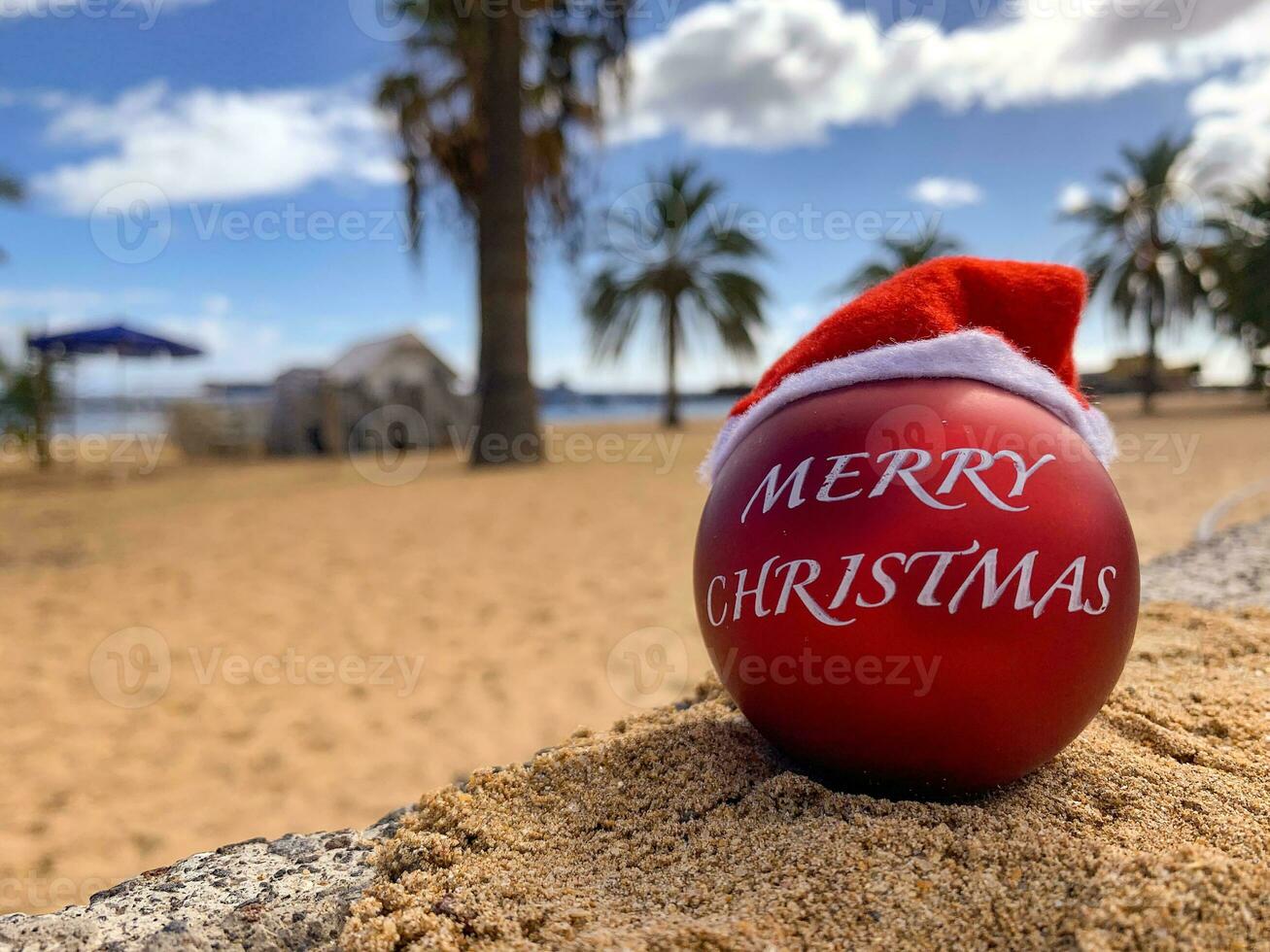 bomba de navidad en el sombrero de santa en la playa tirada en la arena con palmeras y cielo azul en el fondo. feliz navidad desde el paraíso, isla exótica. hawai, islas canarias, bali. foto