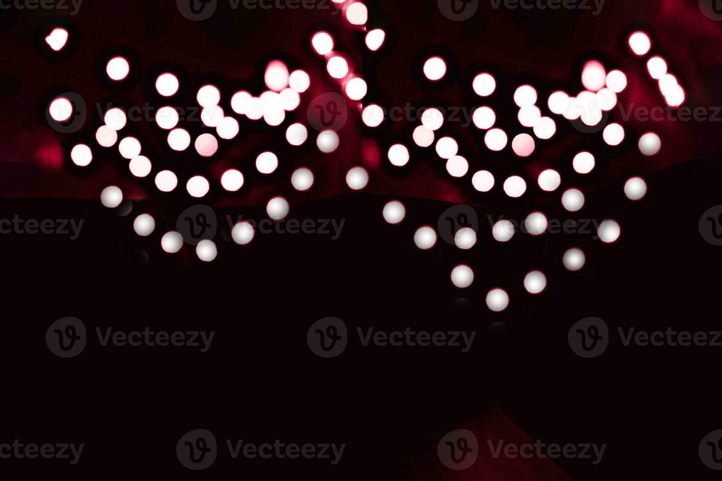 Blurry garland lights on a dark background. Festive Christmas and New Year background. Soft focus. Image toned in color of the year 2023 viva magenta photo