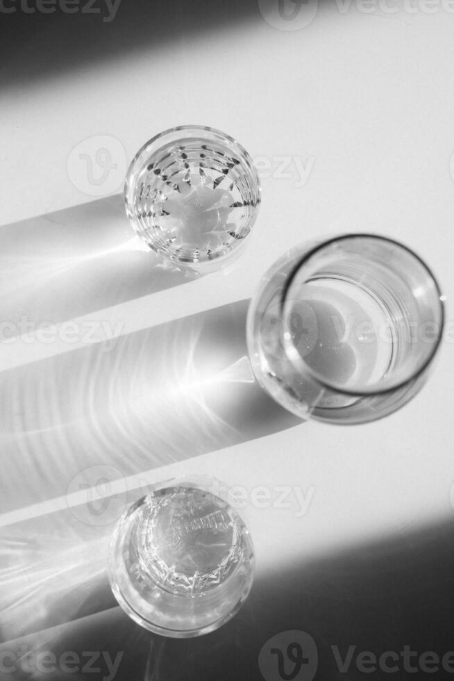 Water in glasses and in a vase on white steel. Shadows, hard light. photo
