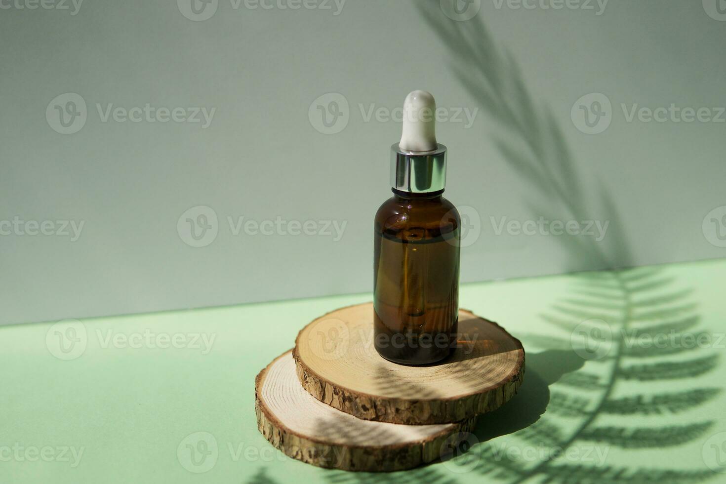 Cosmetic bottle with facial serum on a wooden podium. The concept of zero waste and ecology. A hard shadow from a fern leaf. photo