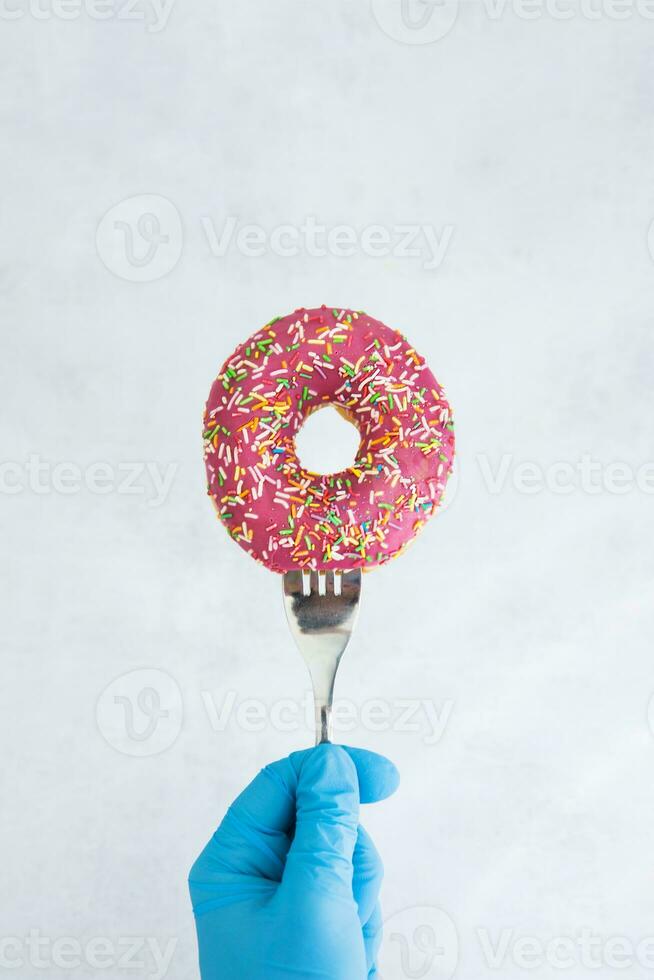 The doughnut is impaled on a fork. Hand in a medical glove on a light background. The concept of coronavirus. photo