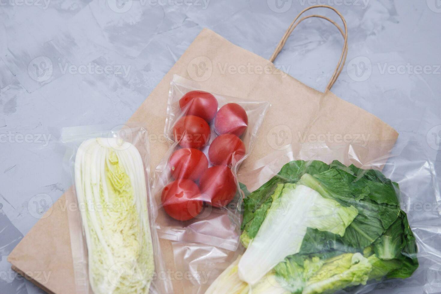 Tomatoes, lettuce leaves and Peking cabbage in a vacuum package. A set for delivering food for dinner on a gray background. photo