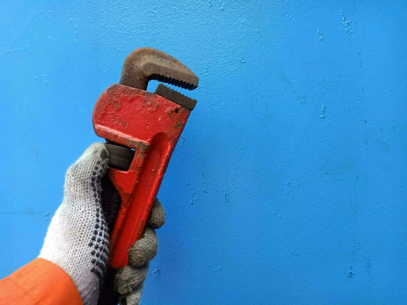 Plumbing wrench in male hand using handglove isolated on blue. Rustic pipe wrench or monkey wrench photo