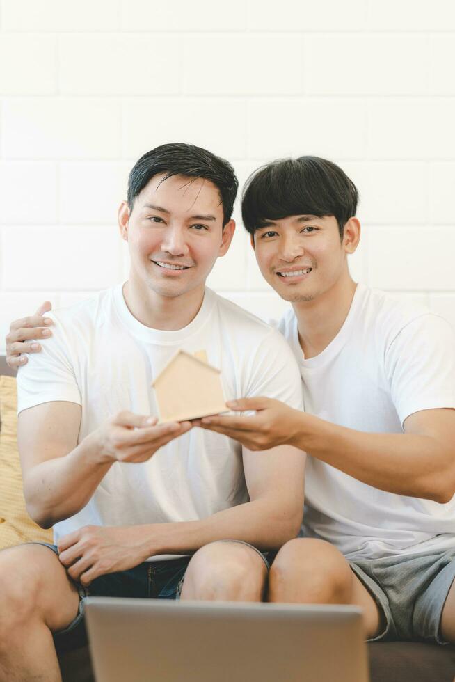 Asian Gay Couple Buying New Dream House Or Property with house model. Concept for marriage, loan, finance, insurance, mortgage, real estate and property. photo
