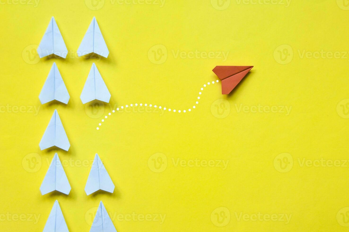 Red paper airplane origami leaving other white airplanes on yellow background with customizable space for text or ideas. Leadership skills concept and copy space photo