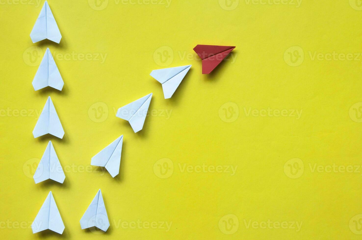 Red paper airplane origami leaving with other white airplanes on yellow background with customizable space for text or ideas. Leadership skills concept and copy space photo