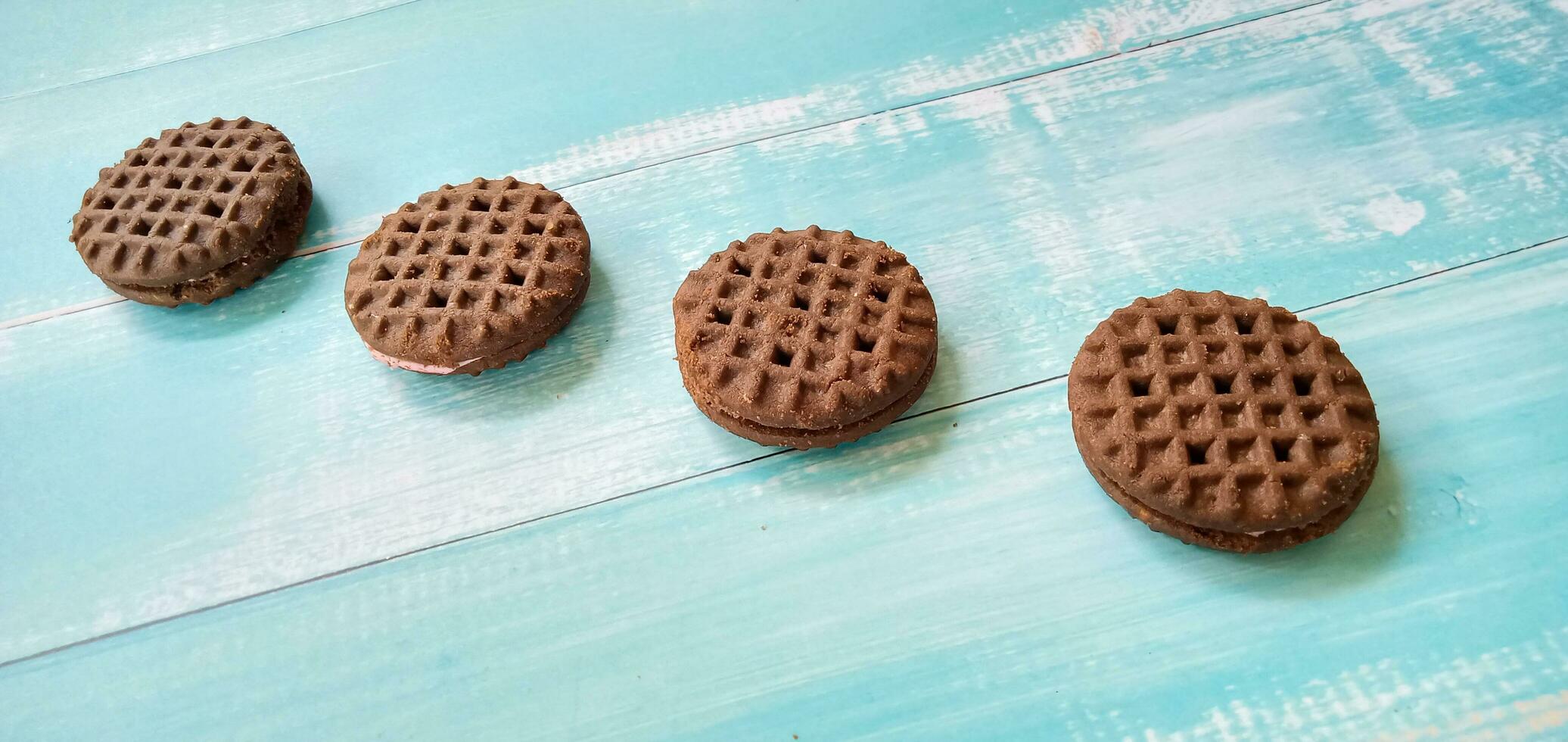 Chocolate sandwich cookies on blue background. Pile of sandwich chocolate cookies with a sweet cream is the best selling dessert. photo