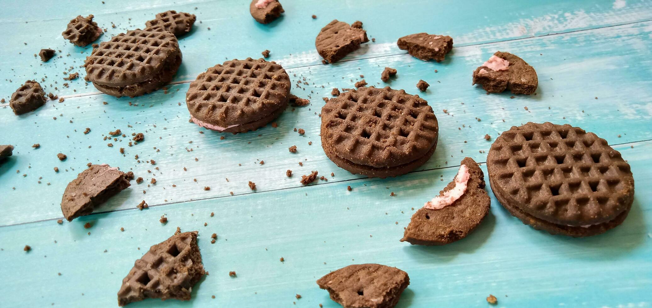 Chocolate sandwich cookies with crumbs on blue background. Pile of sandwich chocolate cookies with a sweet cream is the best selling dessert. photo