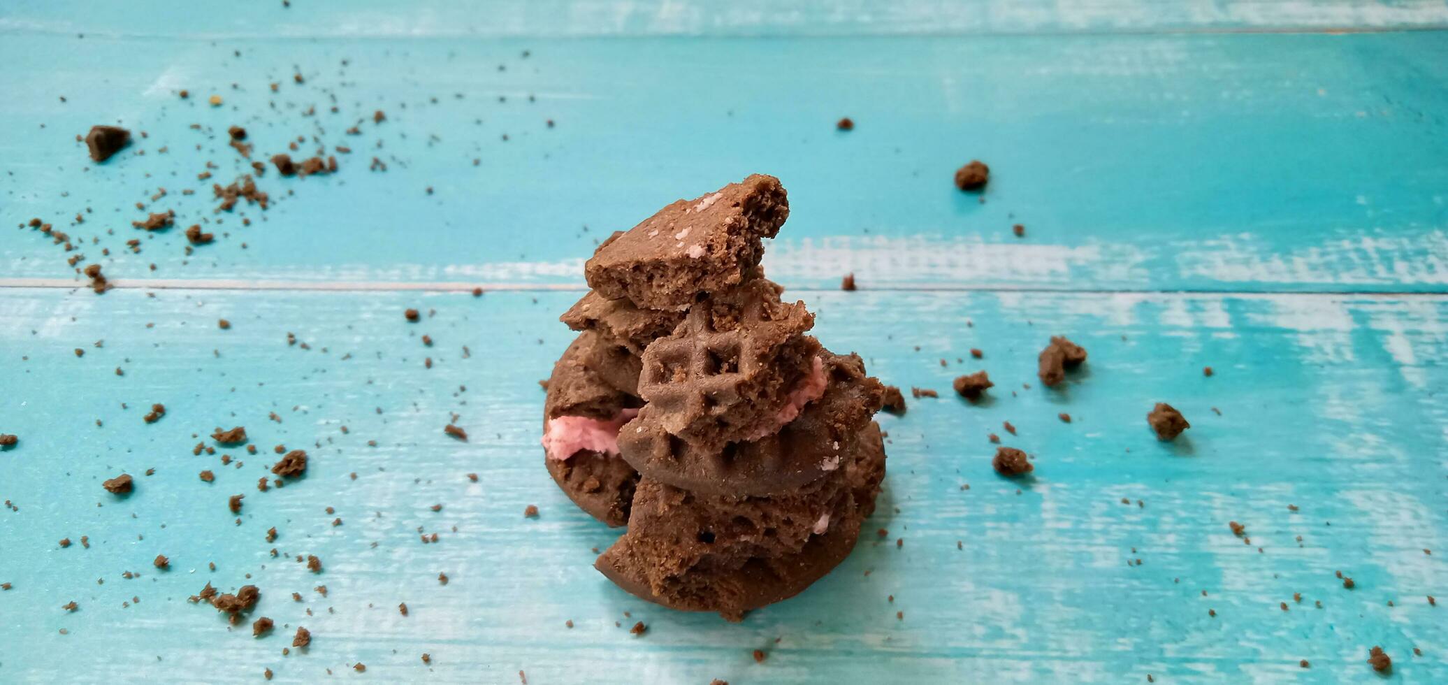 Crumbs of chocolate sandwich cookies on blue background. Pile of sandwich chocolate cookies with a sweet cream is the best selling dessert. photo