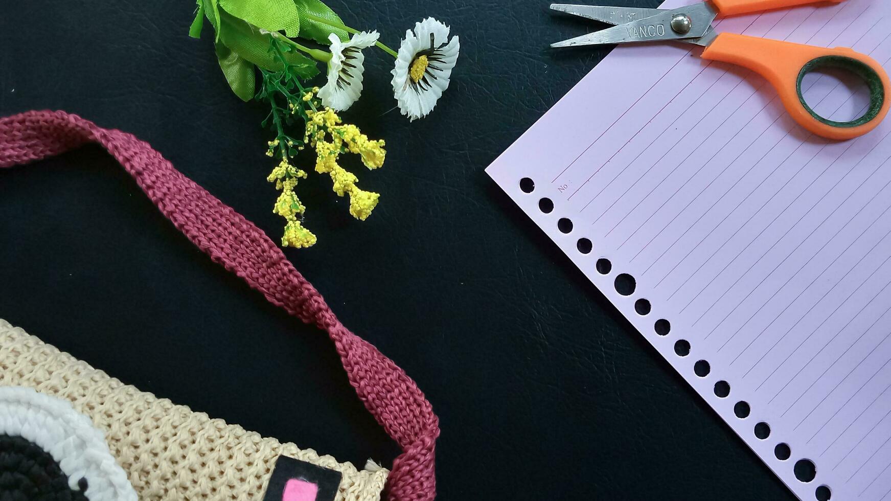 Pink notebook, scissors, flowers, and bag are on a black background as an elegant background. Education concept, business concept, blank document, blank paper. photo